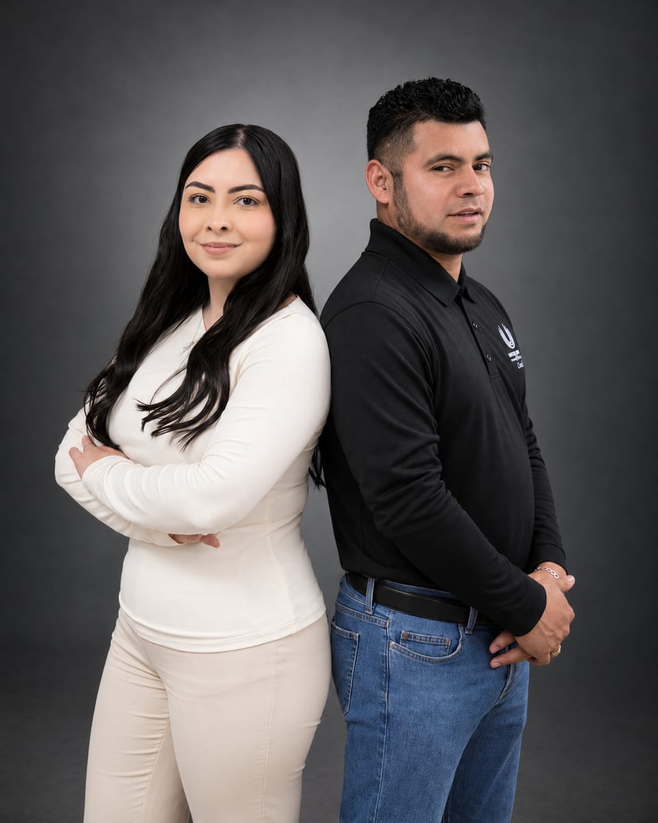 A woman in a cream top with arms crossed and a man in a black UFG polo stand back to back on a dark grey backdrop