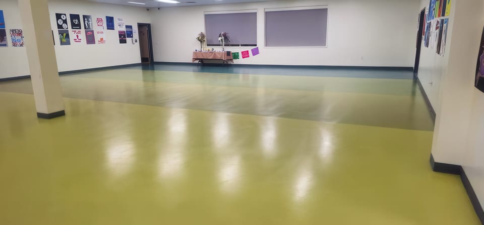 A freshly polished olive-green school hall floor with student posters on the walls and a decorated table at the back