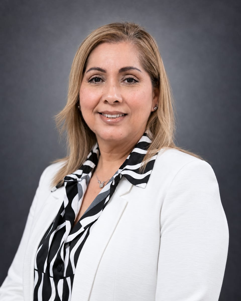Portrait of a smiling woman with blonde hair in a white blazer over a black-and-white print blouse on grey