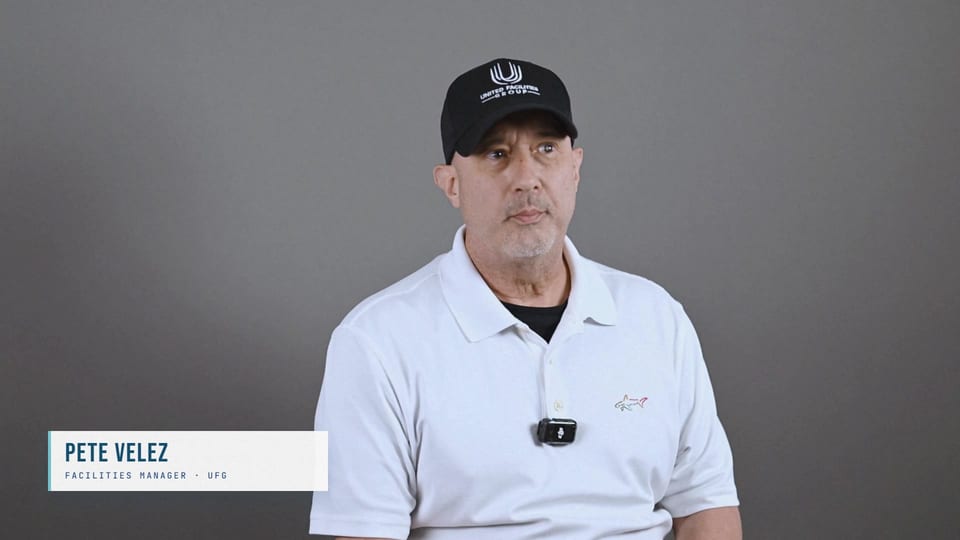 Pete Velez seated in a black UFG cap and white polo, looking aside, a frame from the film Coaches, Not Supervisors